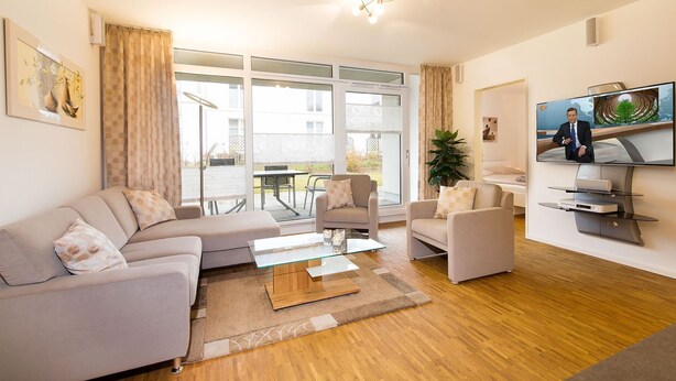 A modern living room with a sofa, chairs, a coffee table, and a flat-screen TV. - Dünenresort Binz - Apartment 4.1.6 (Binz)