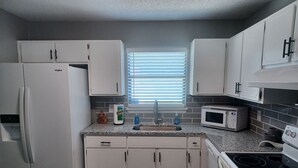 Una cocina compacta con armarios blancos, un refrigerador, un microondas y una estufa.