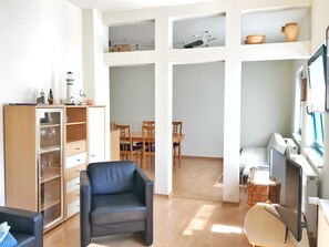 Amplia sala de estar con un sillón de cuero negro, un aparador de madera con puertas de cristal, una mesa de comedor con sillas y un escritorio con monitor.