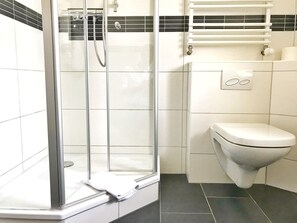 Un baño con cabina de ducha de vidrio, inodoro y barra para toallas.