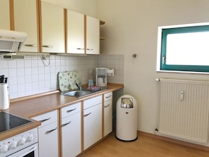 A kitchen with white cabinets, a stove, a sink, a coffee maker, and a trash bin.