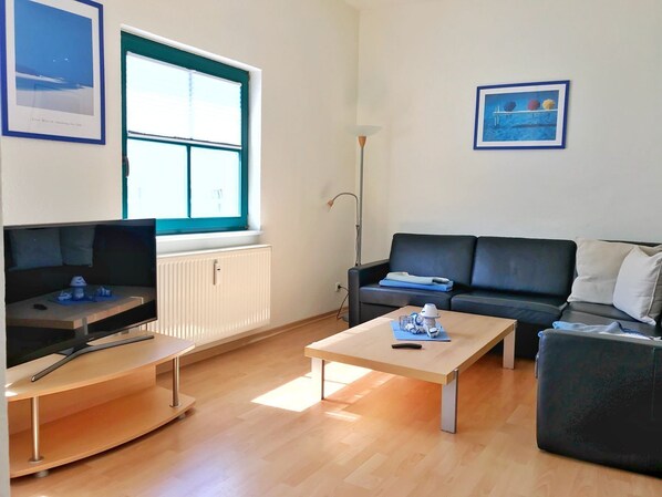 Una sala de estar moderna con un televisor de pantalla plana, un sofá de cuero negro, una mesa de centro de madera y un sillón negro.