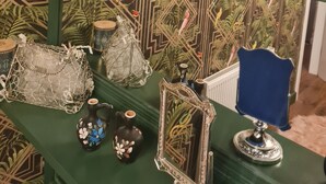 Een presentatie van decoratieve objecten, waaronder een klok, beeldjes en glaswerk, op planken voor een behang met een patroon.