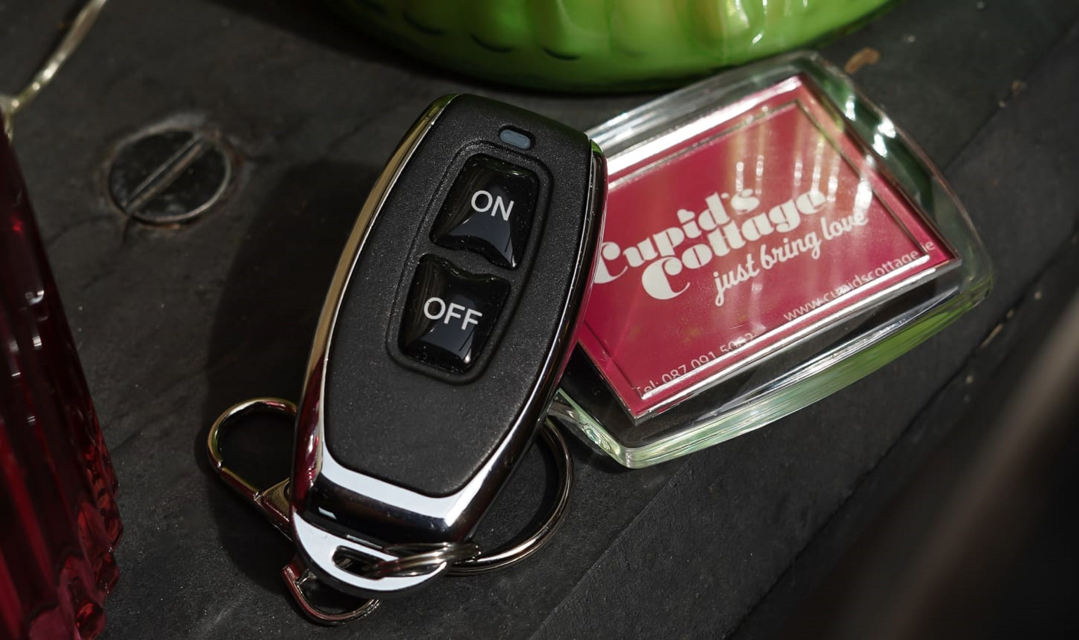 A car key fob with an 'ON' and 'OFF' switch, a key ring, and a red booklet titled 'Cupid's Collage just bring love'.