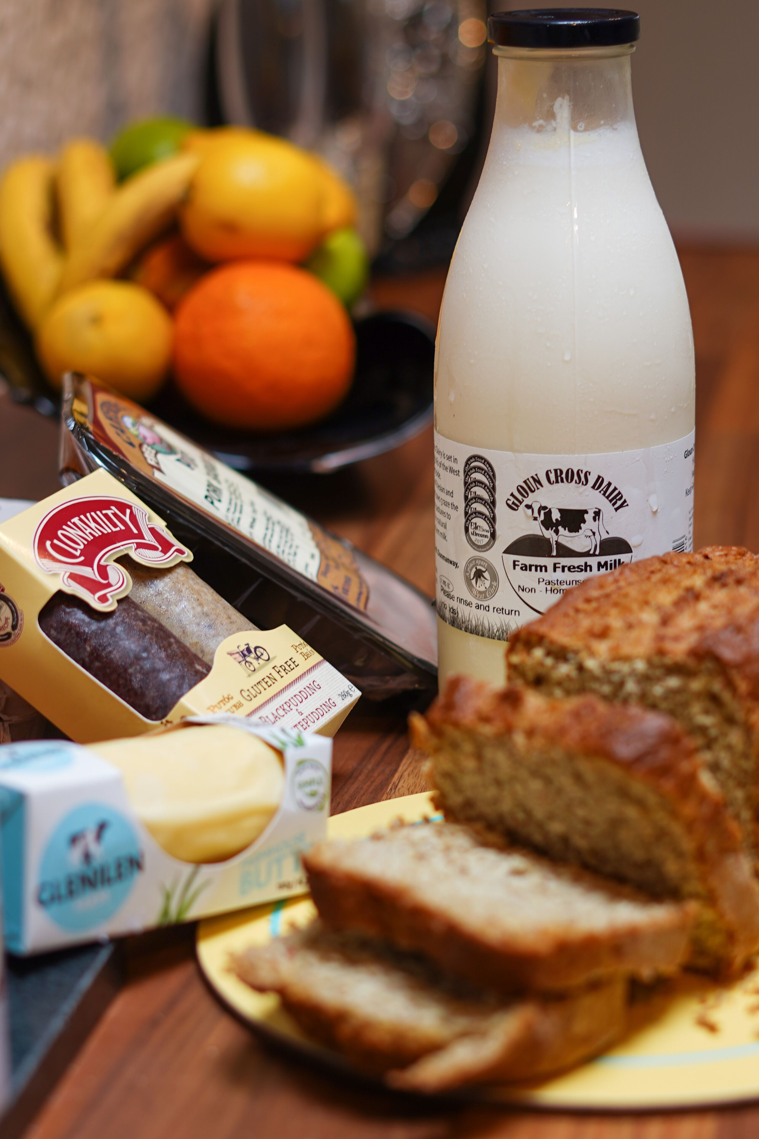 A table with sliced bread, a bottle of milk, a box of cheese, and a bowl of fruit.