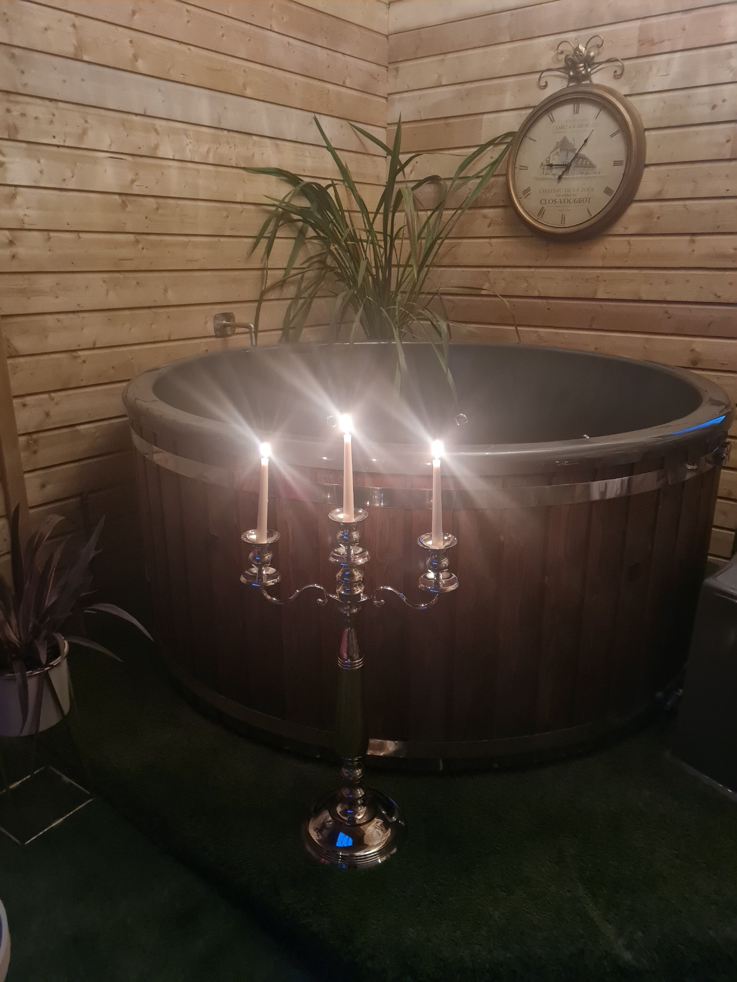 Una habitación de madera con una bañera de madera grande, un reloj en la pared y un candelabro con velas.
