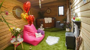 Een knus interieur met houten details, een klein rond tafeltje met een bloevas, een roze plufzak en een klein, zacht vloertje.