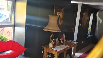 Una habitación con una pared oscura, una silla roja, una mesa de madera con una lámpara y un espejo.