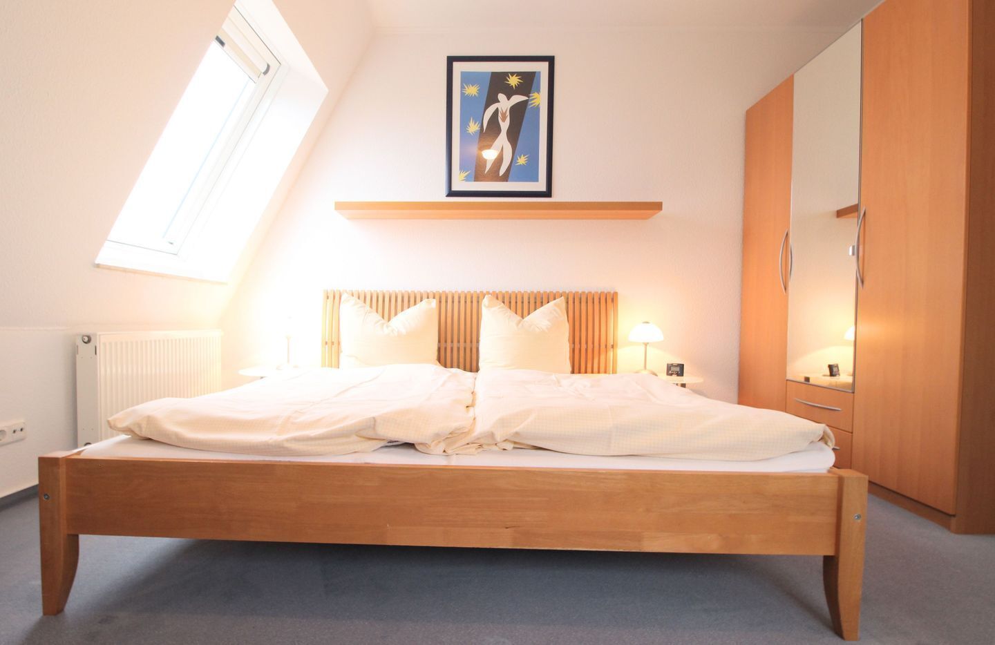 Ein Schlafzimmer mit einem hölzernen Bett, einem Oberlicht, einem gerahmten Kunstwerk über dem Bett und einem Spiegel an der Wand.