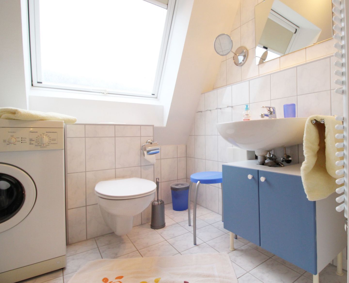 A compact bathroom with a washing machine, toilet, sink, and a small window.