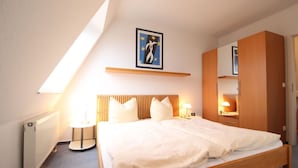A bedroom with a bed, bedside tables, a radiator, a ceiling light, a framed picture, and a wardrobe.