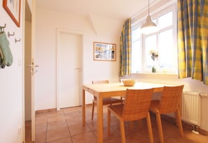A dining area with a wooden table and wicker chairs, a framed picture on the wall, and a window with curtains.