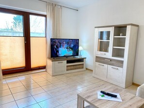 Una habitación con un televisor sobre un mueble de madera, una mesa con un control remoto y un armario con puertas de vidrio.