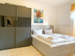 Un dormitorio con cama, un armario gris, un cuadro de flores y un radiador.