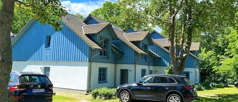 Un bâtiment bleu avec un toit recouvert de tuiles, des voitures garées et des arbres.