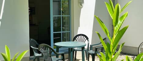 A patio area with a table and chairs, a door leading to an interior space, and a small garden area with plants.