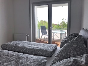 Ein Schlafzimmer mit einer großen Schiebeglastür, die auf einen Außenbalkon mit Tisch und Stuhl führt.