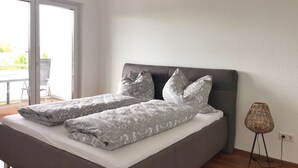 Une chambre moderne avec un grand lit, une literie grise et une vue sur l’extérieur grâce à une porte-fenêtre coulissante.