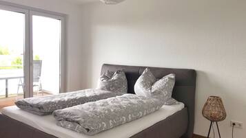 Een moderne slaapkamer met een groot bed, grijs beddengoed en uitzicht op het natuur door een schuifdeur.'