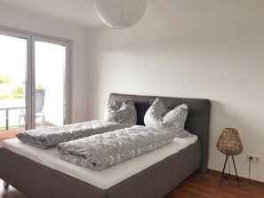Une chambre moderne avec un grand lit, une literie grise et une vue sur l’extérieur grâce à une porte-fenêtre coulissante.