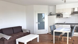 A modern living room with a brown sofa, a white coffee table, and a dining area with a table and chairs. - Ferienappartement "langschläfer" (Sassnitz)