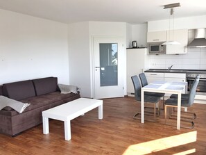 Un salon moderne avec un canapé marron, une table basse blanche et un coin repas comprenant une table et des chaises.