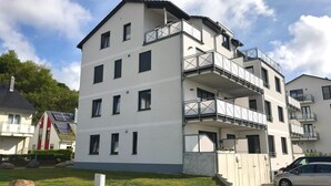 A multi-story residential building with balconies, a paved driveway, and a car parked in front. - Ferienappartement "langschläfer" (Sassnitz)