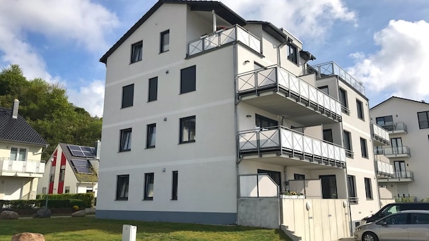 Un immeuble résidentiel à plusieurs étages, doté de balcons, d’une allée pavée et d’une voiture garée devant.