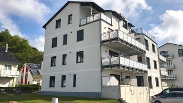 A multi-story residential building with balconies, a paved driveway, and a car parked in front.