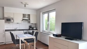 A modern kitchen with white cabinets, a microwave, stove, and a dining area with a table and chairs. - Ferienappartement "langschläfer" (Sassnitz)