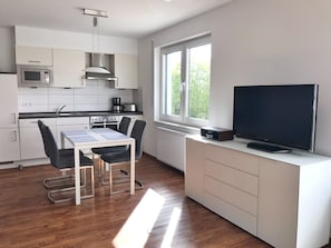 A modern kitchen with white cabinets, a microwave, stove, and a dining area with a table and chairs. - Ferienappartement "langschläfer" (Sassnitz)