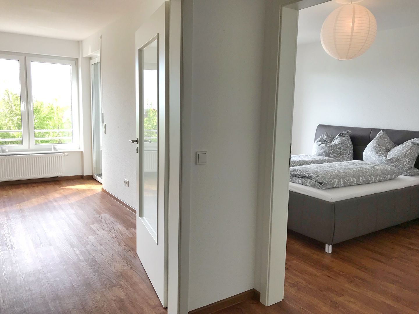 Ein modernes Schlafzimmer mit großem Fenster, einem Bett mit gemusterten Betttextilien und einer hängenden Leuchte.