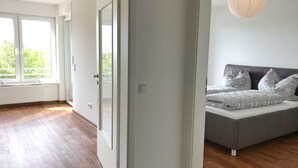 Une chambre moderne avec une grande fenêtre, un lit recouvert d’une literie à motifs et un luminaire suspendu.