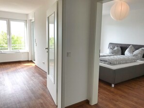 Ein modernes Schlafzimmer mit großem Fenster, einem Bett mit gemusterten Betttextilien und einer hängenden Leuchte.