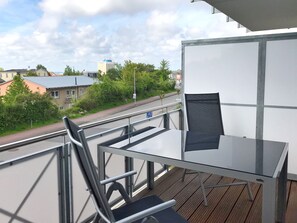 A balcony with a table and chairs, overlooking a street with buildings and trees.