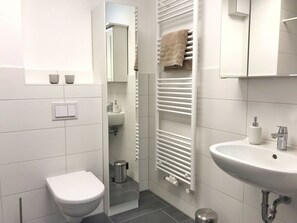 Une salle de bain moderne équipée de toilettes, d’un lavabo, d’un porte-serviettes et d’un miroir.