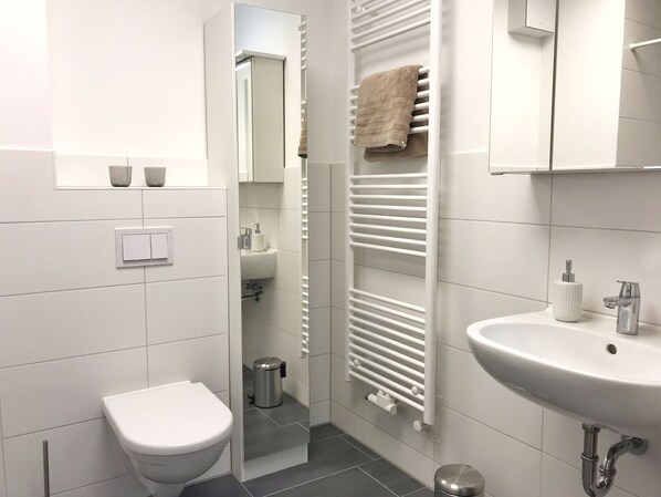 A modern bathroom with a toilet, sink, towel rack, and a mirror.