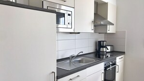 Une cuisine moderne avec des armoires blanches, un four à micro-ondes en acier inoxydable, une machine à café, un évier et un four.