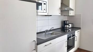 A modern kitchen with white cabinets, a stainless steel microwave, a coffee maker, a sink, and an oven.