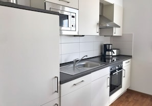 Moderni keittiö, jossa on valkoiset kaapit, ruostumattomasta teräksestä valmistettu mikroaaltouuni, kahvinkeitin, pesuallas ja uuni.