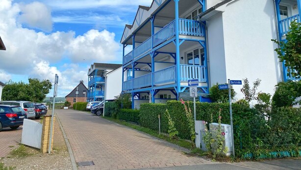 A residential building with a blue balcony, a clear sky, and parked cars along the street. - Ferienwohnung "osterholz" (Baabe)