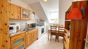 A compact kitchen with wooden cabinets, a microwave, a kettle, and a sink. - Ferienwohnung "osterholz" (Baabe)