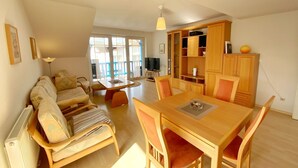 A spacious living area with a sofa, dining table, and wooden cabinets. - Ferienwohnung "osterholz" (Baabe)