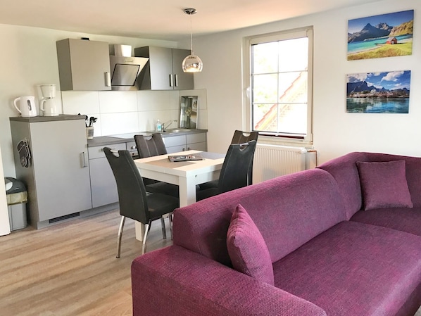 A modern kitchen with grey cabinets, a dining table with chairs, and a purple sofa in the living area.
