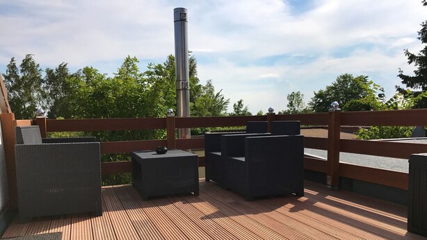 A wooden deck with outdoor furniture, a metal chimney, and a wooden fence.