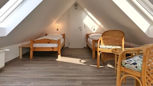 A small attic bedroom with two wooden beds, a wicker chair, and skylights.