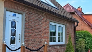 A brick building with a white door and window, a small staircase, and potted plants.