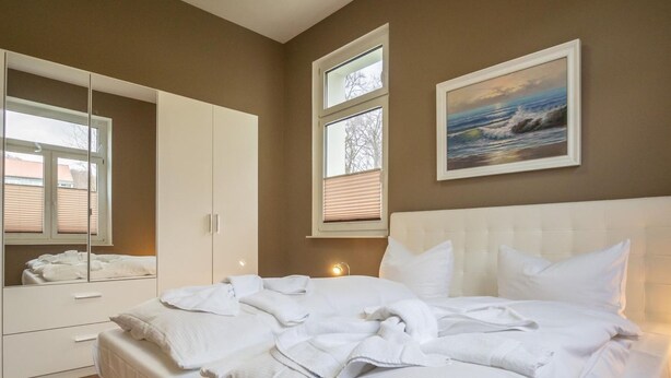 Een slaapkamer met een bed, een kledingkast, een raam en een schilderij aan de muur.
