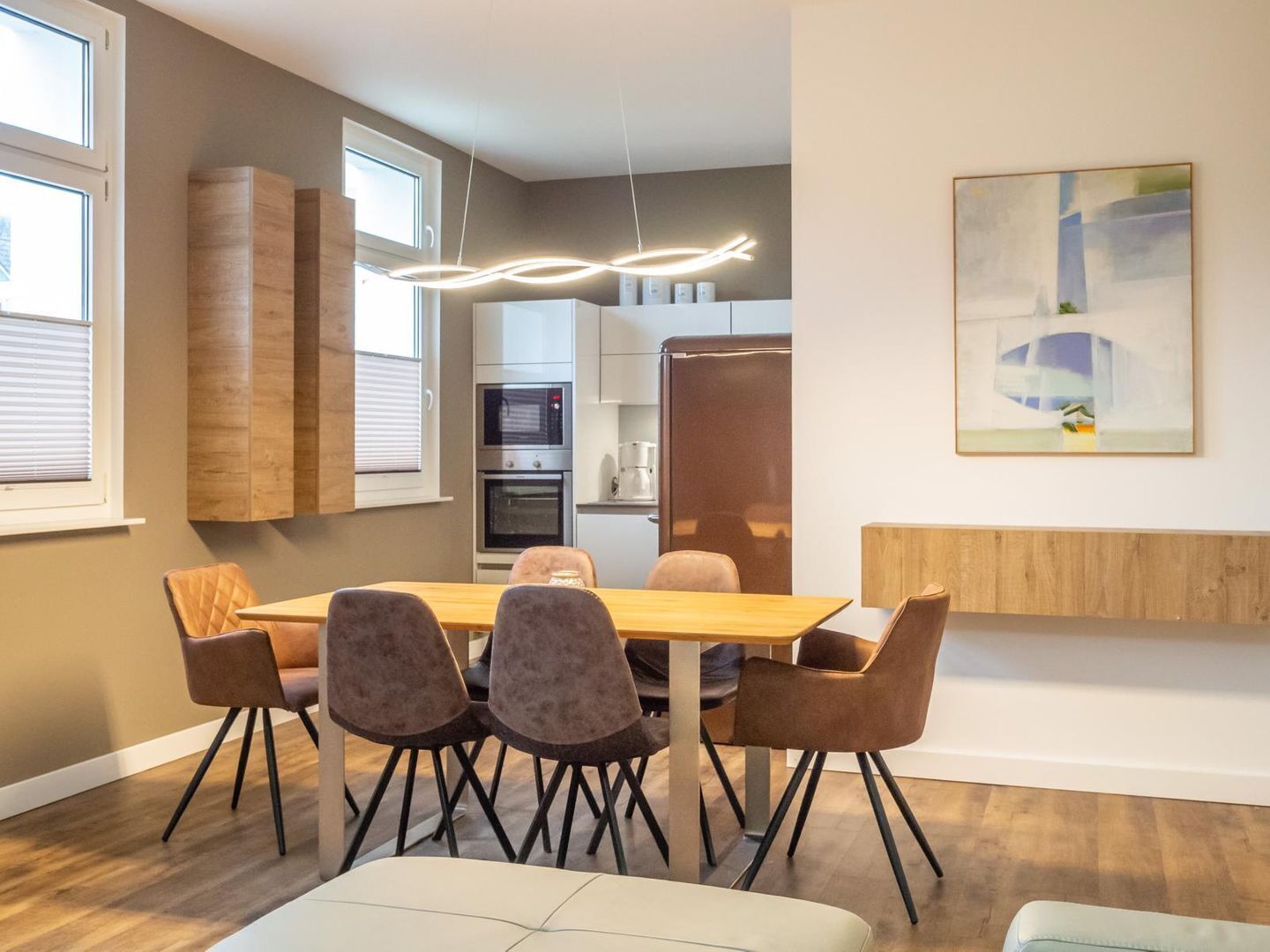 A modern kitchen with built-in appliances, a dining area with a wooden table and chairs, and a contemporary pendant light.