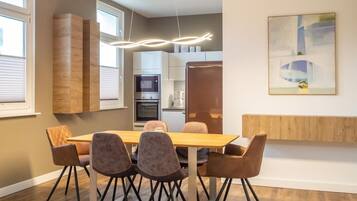 A modern kitchen with built-in appliances, a dining area with a wooden table and chairs, and a contemporary pendant light.